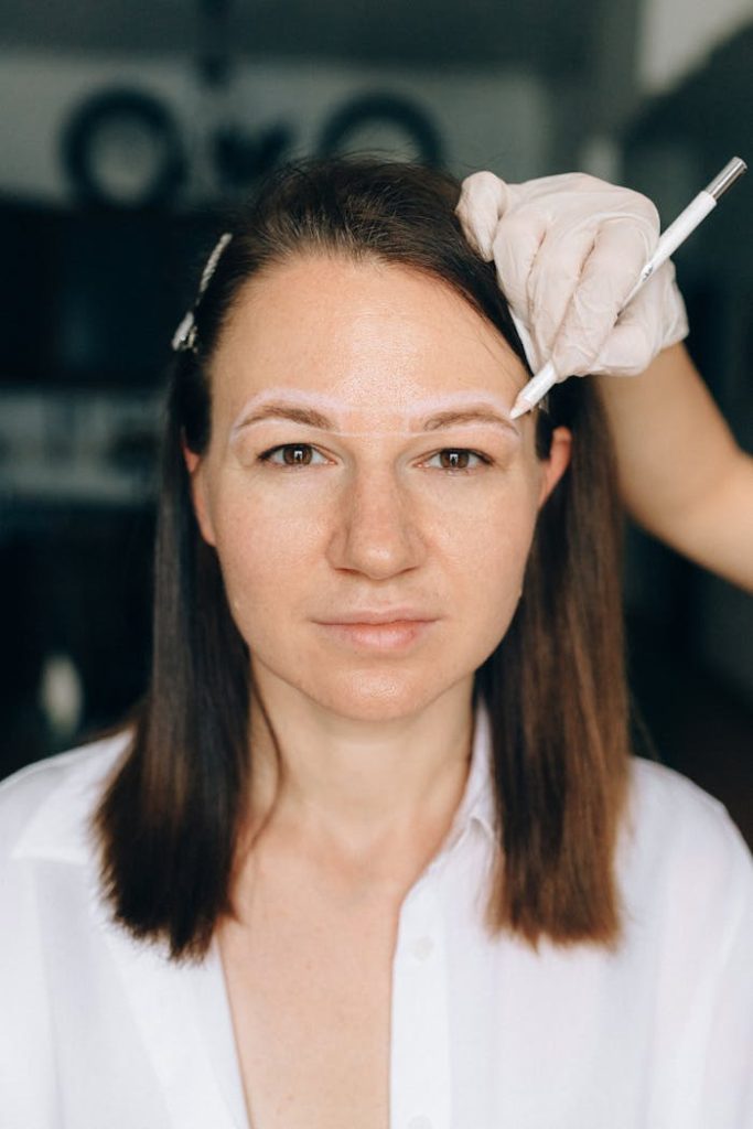 A middle-aged woman receives a cosmetic eyebrow procedure by a professional beautician.